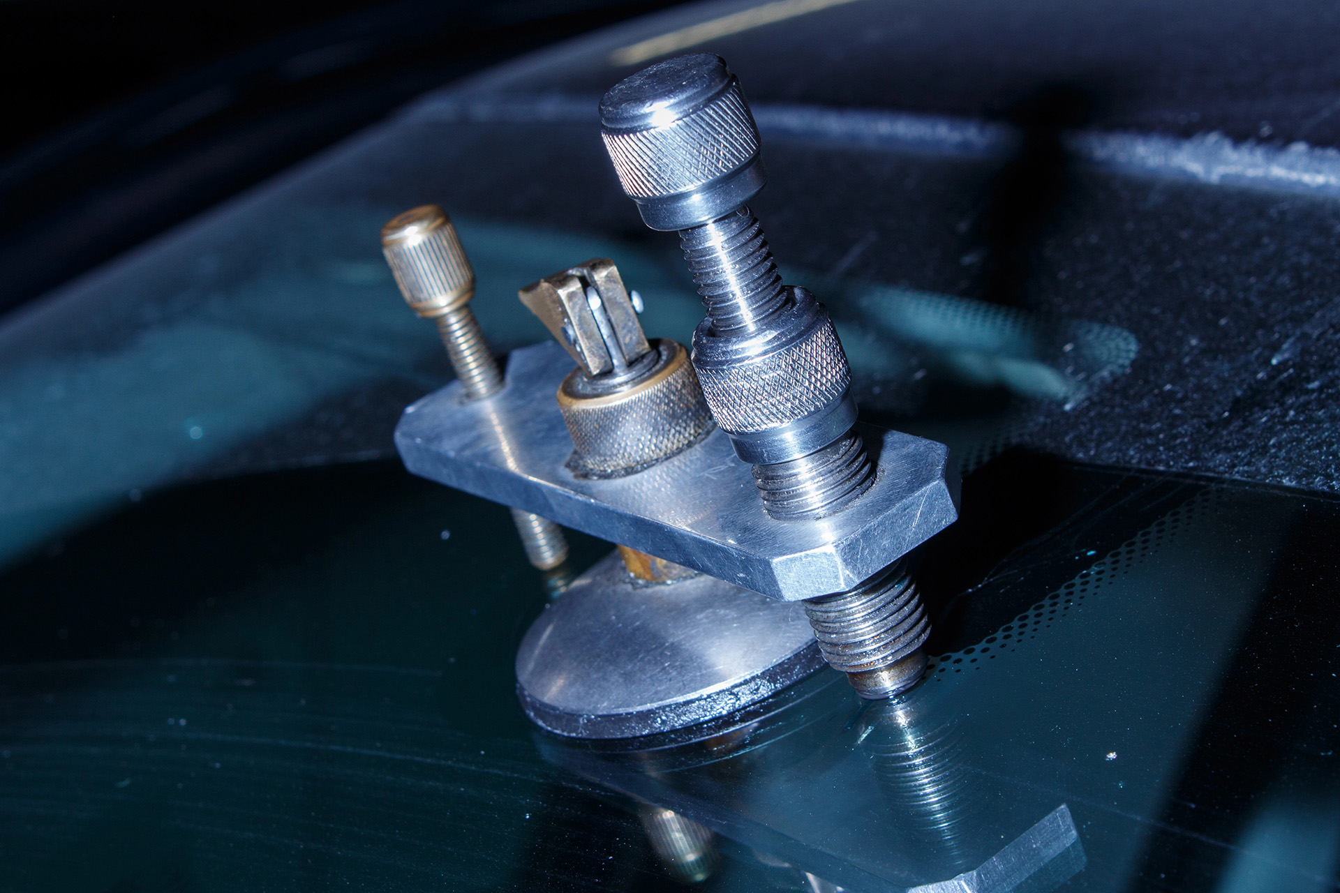 Close-up of a windshield repair tool with metal components and a suction cup, expertly designed for efficient auto glass replacement, attached to a car windshield.