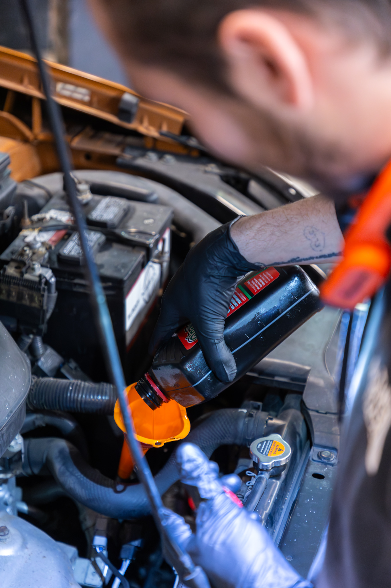 A person, deeply immersed in auto restoration, carefully adds oil to a car engine using a funnel.