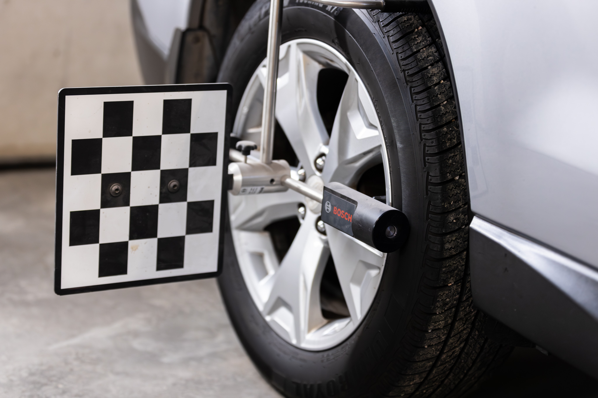 Close-up of a car wheel with a tire alignment checker attached, displaying a black and white checkered calibration pattern, integral to the meticulous process of auto restoration.